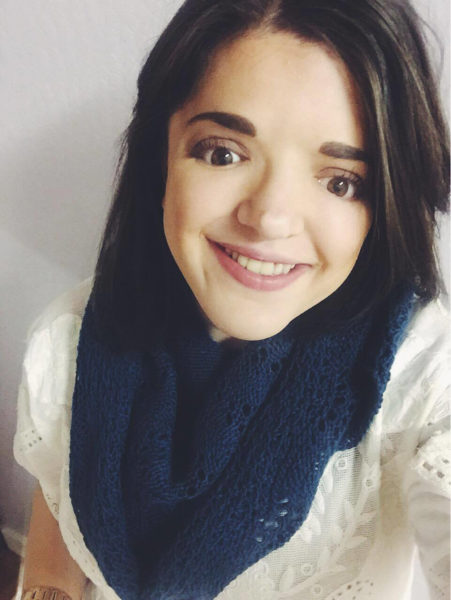 A young woman with dark hair wearing a blue scarf and white top smiles at the camera.