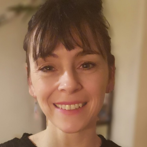 A woman with brown hair tied in a bun on top of her head, smiles at the camera