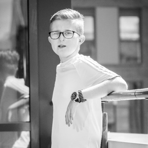 A black and white photo of Sam, who has a cleft lip and palate - he's leaning against a railing