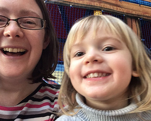 A woman in a striped top smiles next to a young girl with blonde hair.