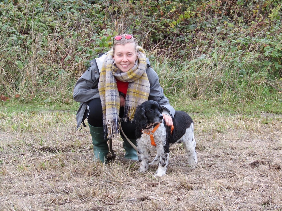 A young blonde woman crouches down next to a black and white dog.