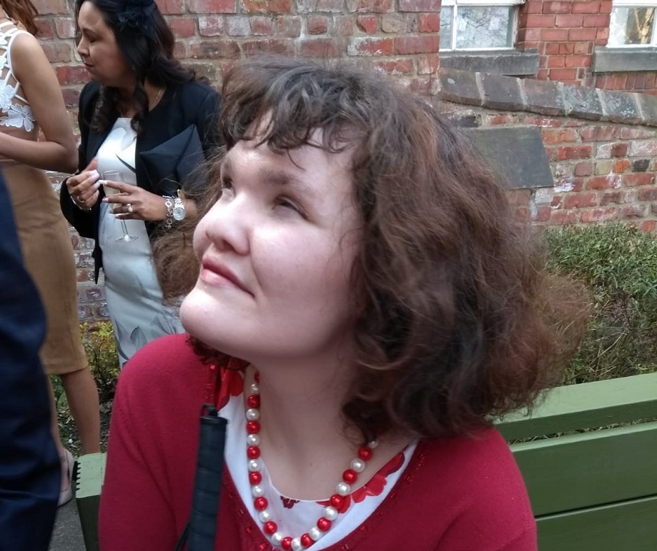 A woman wears a red top, and is sitting in a garden.