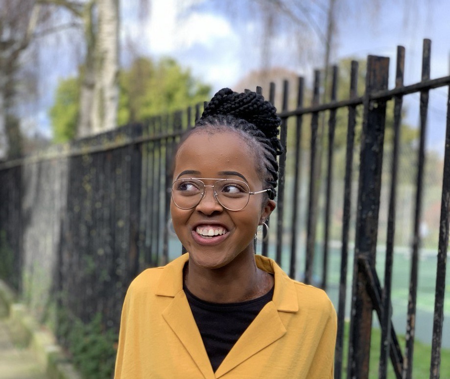 A woman wearing glasses and a bright yellow t-shirt smiles while looking to the left of the camera.