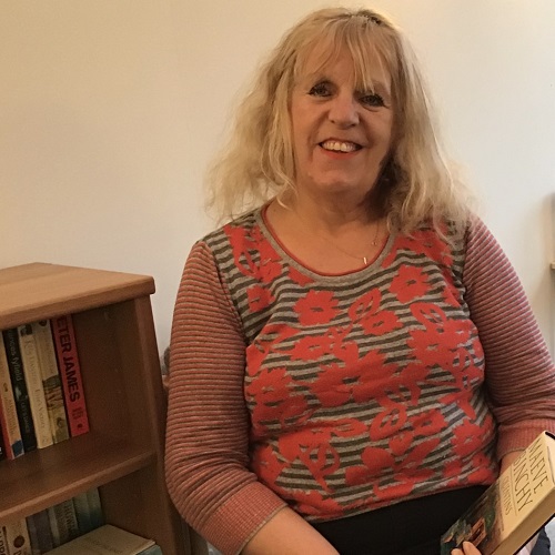 A woman with blond hair wearing a striped top, sits on a chair holding a book