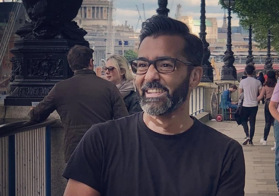 A man with a grey beard and vitiligo on his neck, smiles on London's Southbank.