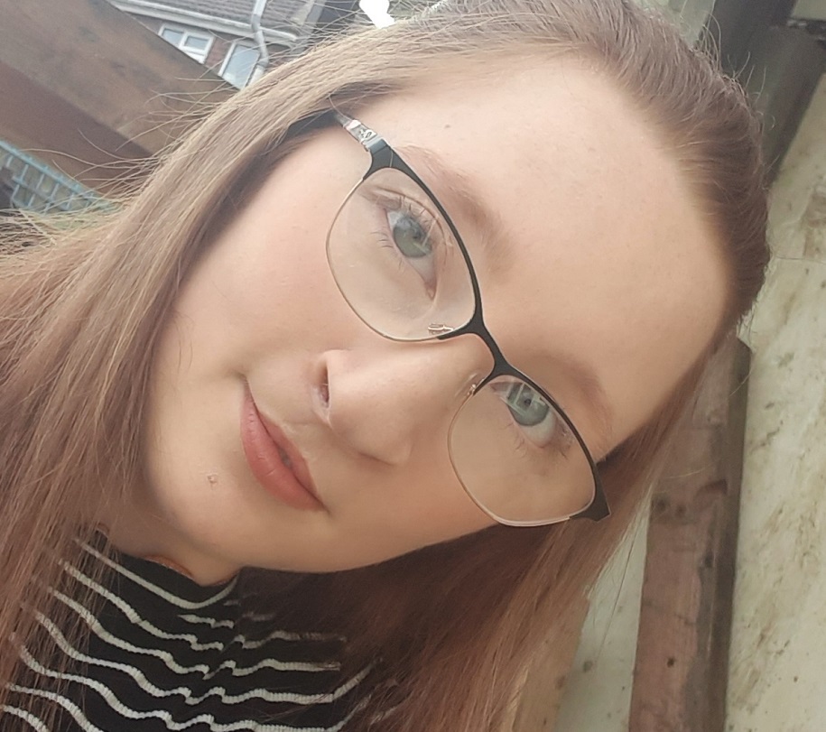 A teenage girl, who has a cleft lip and palate, wears glasses and a striped top.