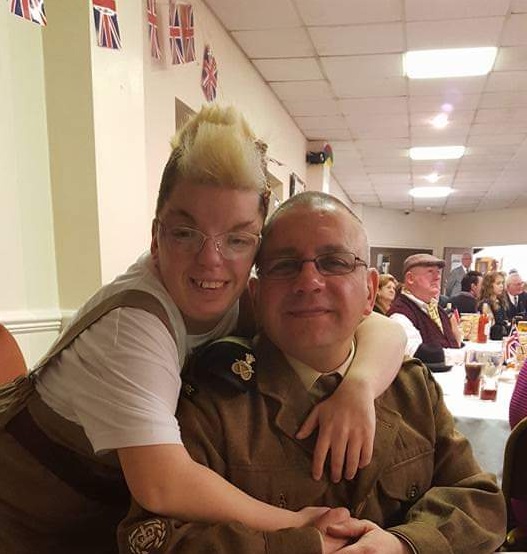 A young woman hugs a man wearing military uniform. They both smile at the camera.