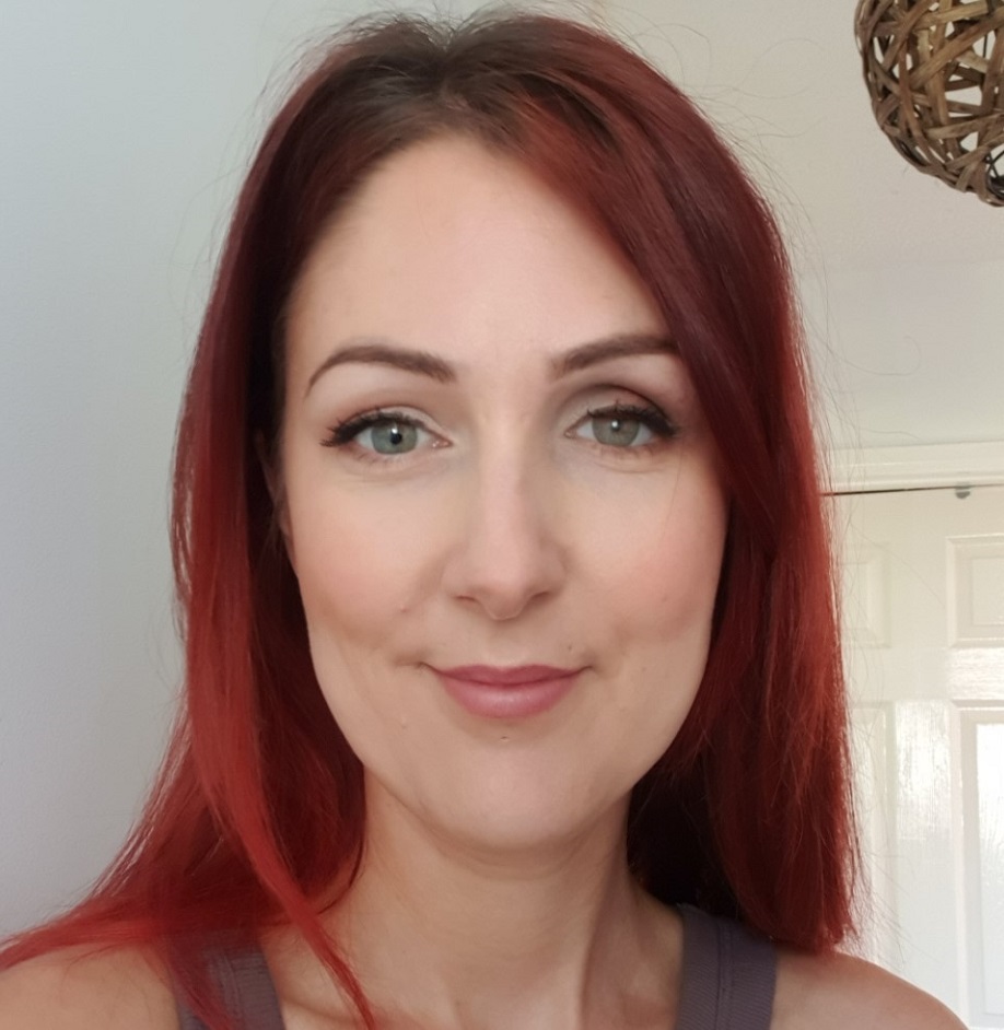 A woman with red hair smiles, against a white background.