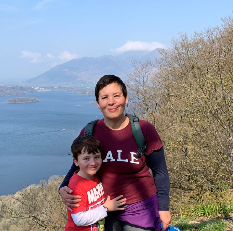 A woman and little boy pose together in front of a beautiful lake and mountain landscape.