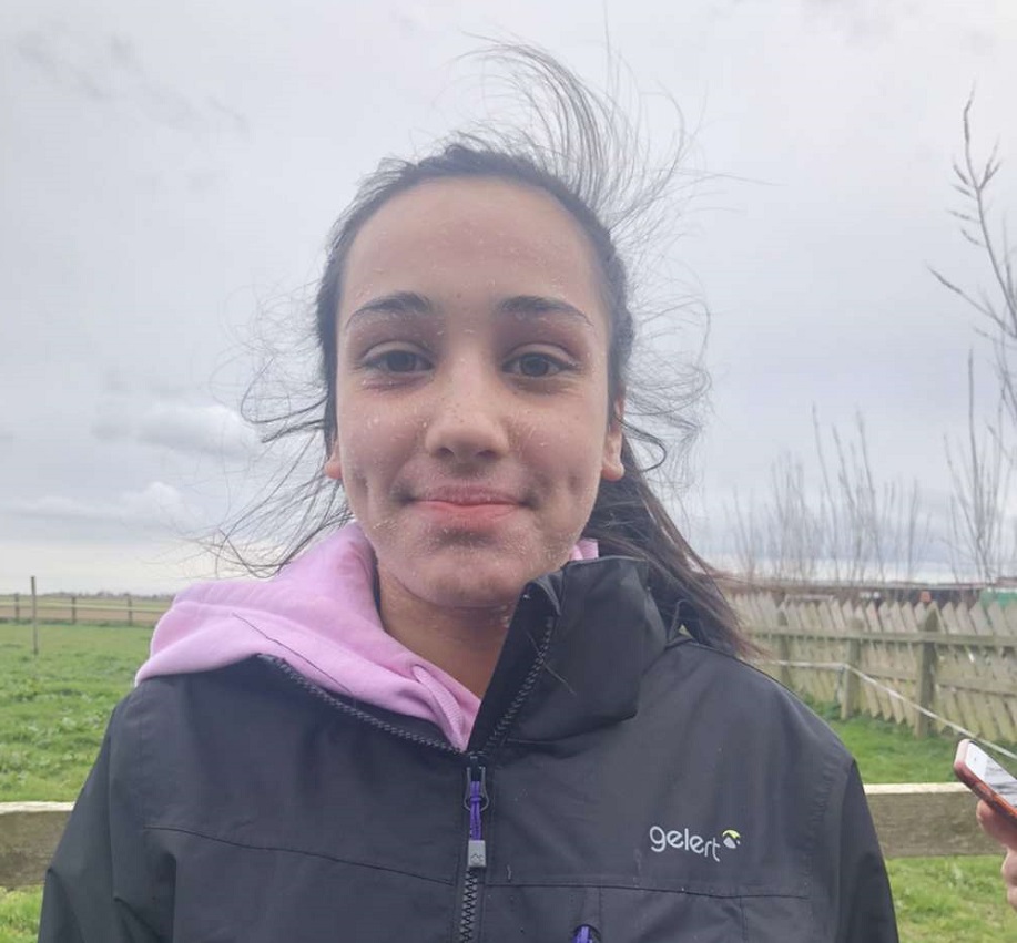 A young girl who has eczema wears a black coat and smiles at the camera. She is outside.