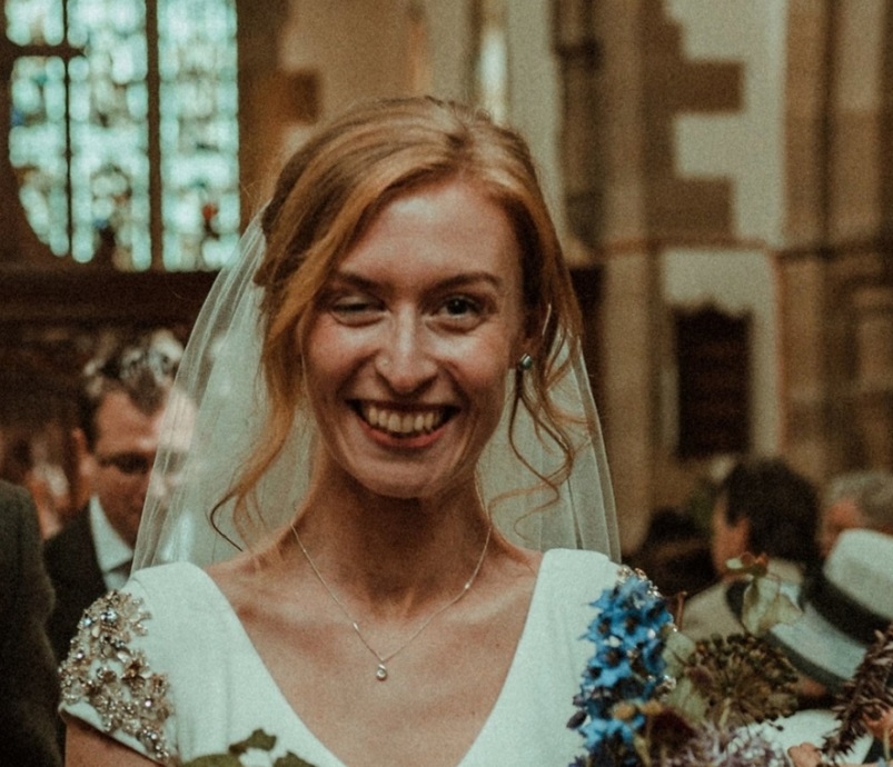 A woman, whose right eye is partially closed due to ptosis, walks down the aisle of a church wearing a bridal dress and veil.