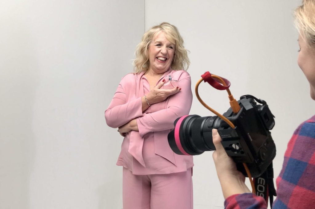 A woman in a pink suit smiles as she has her photograph taken