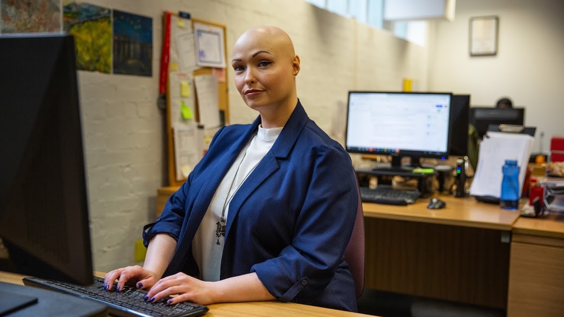 A woman sits at a desk in front of a computer in the workplace