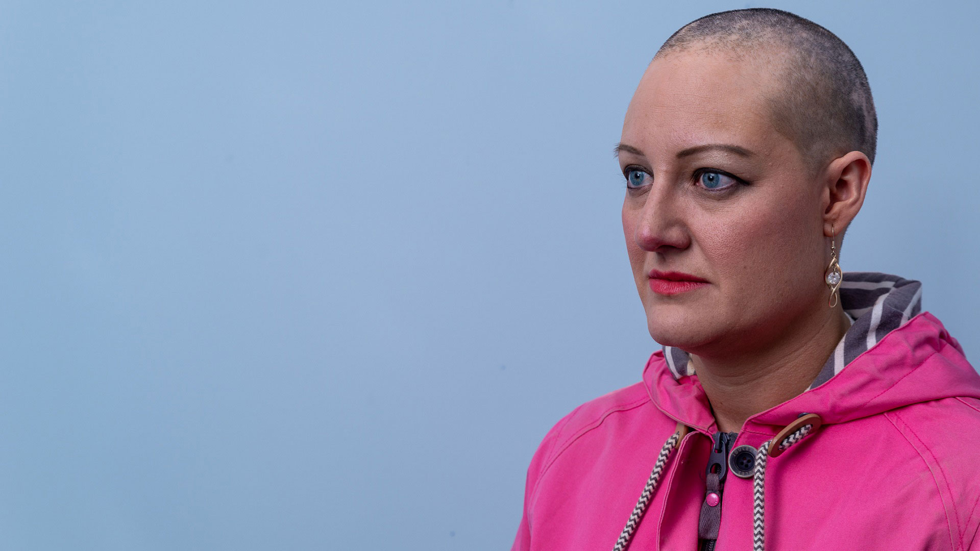 Julie, who has alopecia, against a blue background, looking off camera