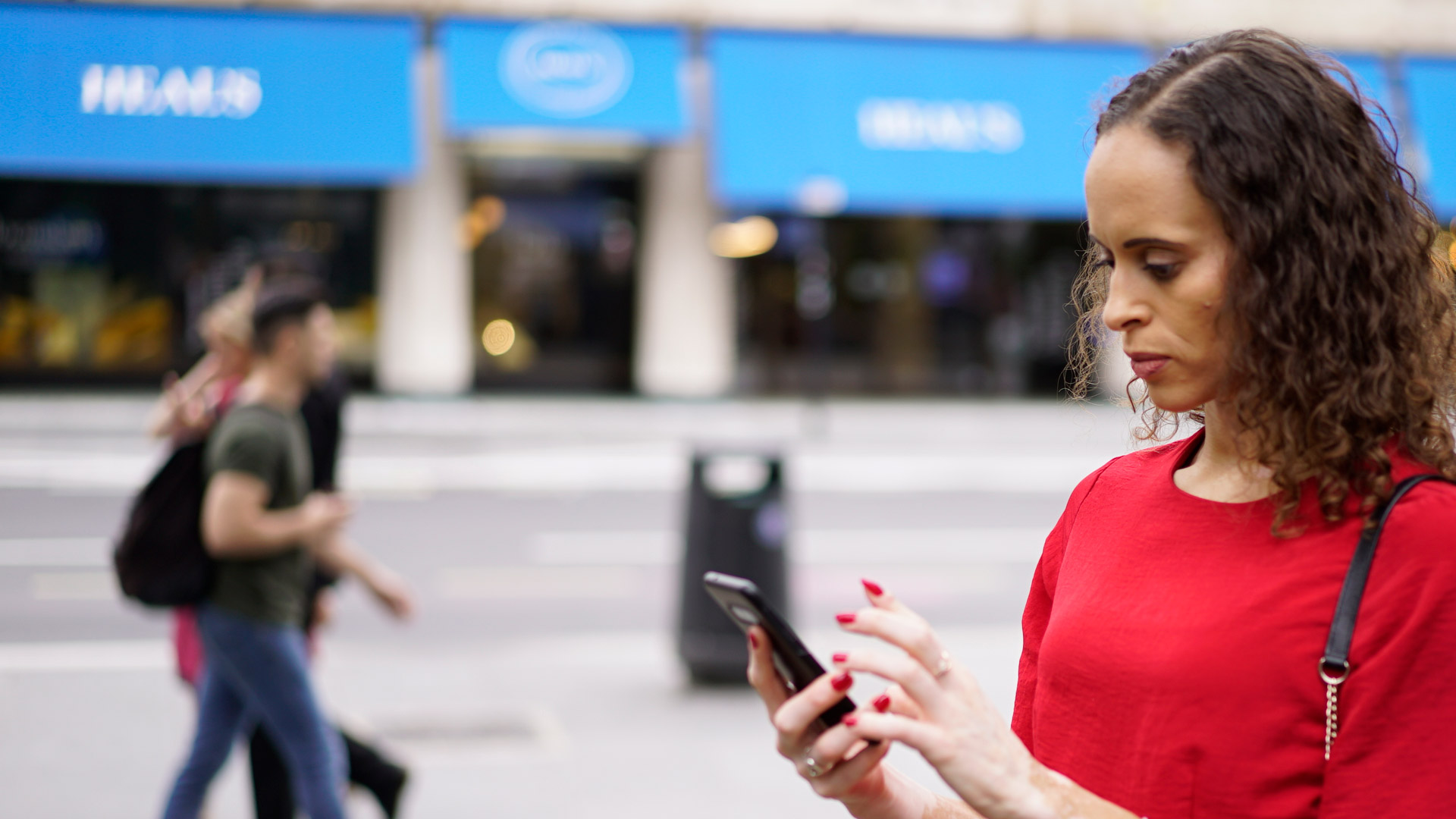 Natalie using a smartphone on the street, with passers-by and shops in the background