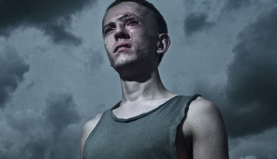 Robert, a young man in his 20s with facial scars, wearing a grey singlet, pictured against a dark sky.