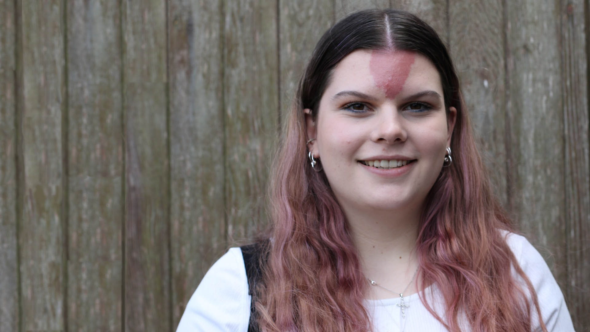 A teenage girl with a triangular-shaped birthmark on her forehead wearing a white t-shirt and smiling.