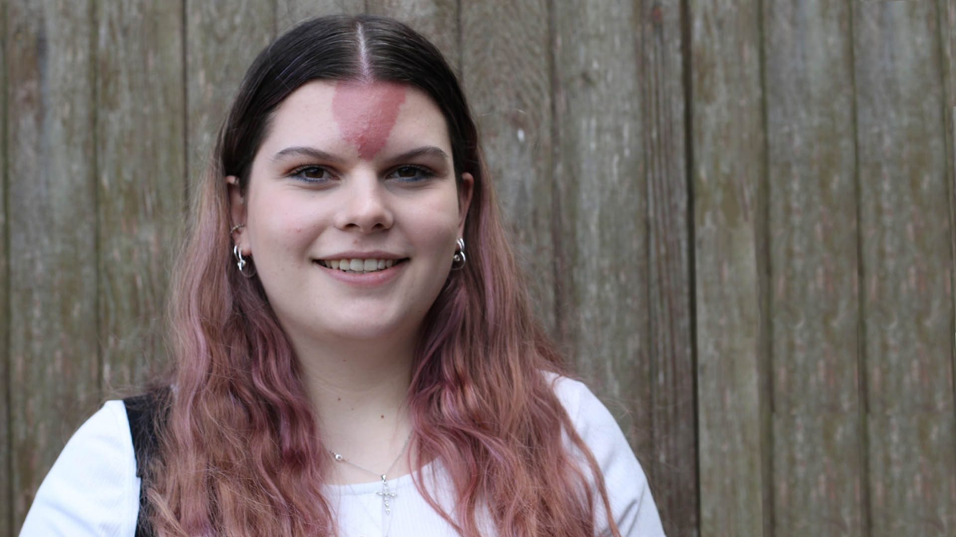 Sophie who has a birthmark on her forehead smiles at the camera wearing a white t-shirt