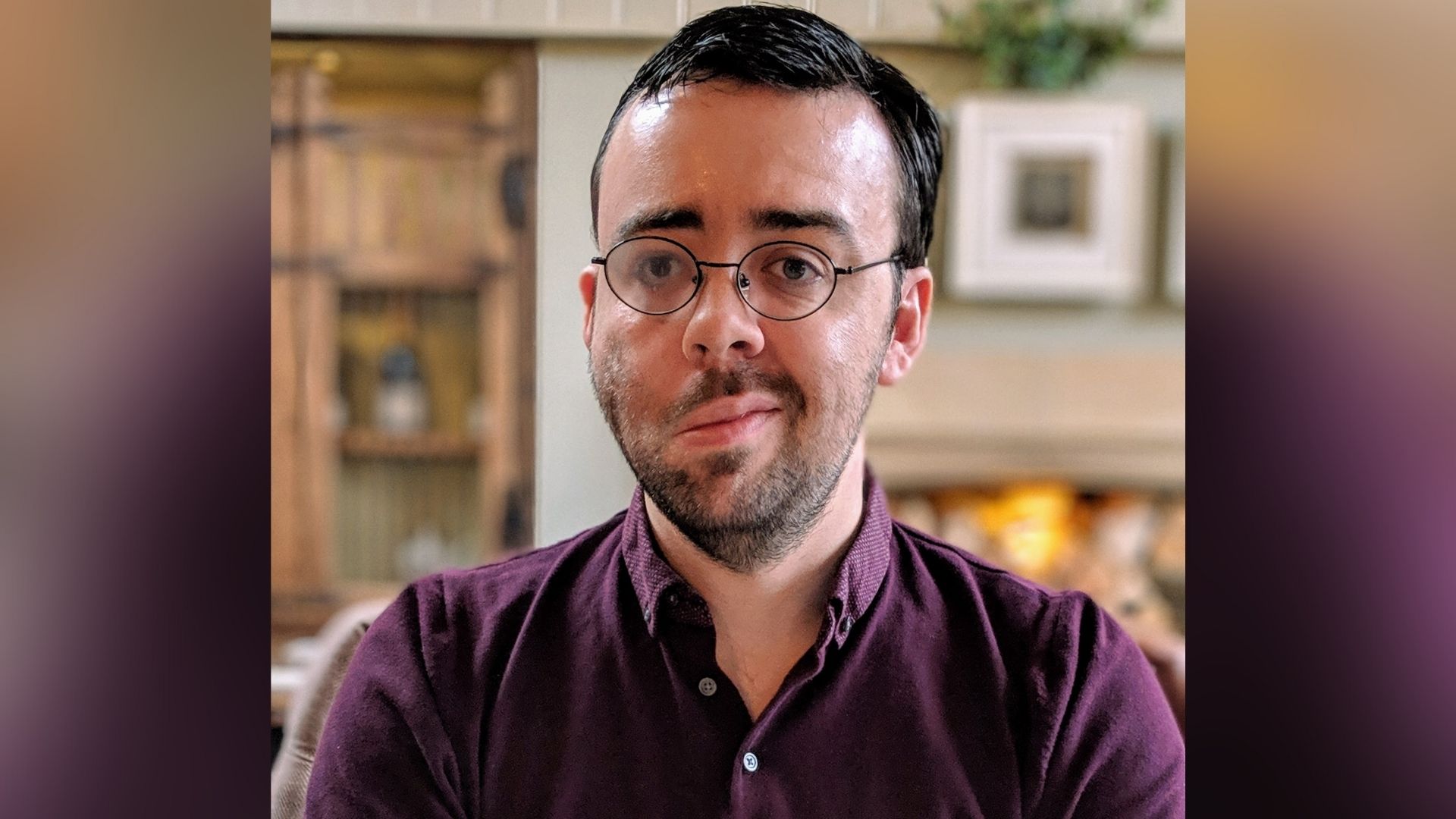 Kevin, a man, 30s, with short dark brown hair, stubble and glasses. The right side of his face droops due to loss of muscle control. He's wearing a purple shirt.