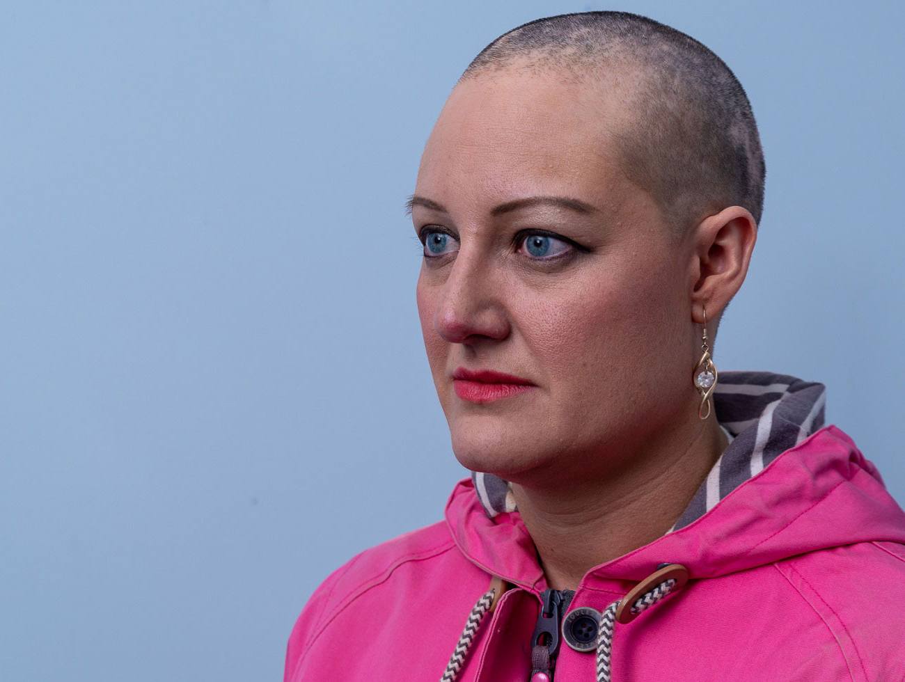 Julie, who has alopecia, against a blue background, looking off camera