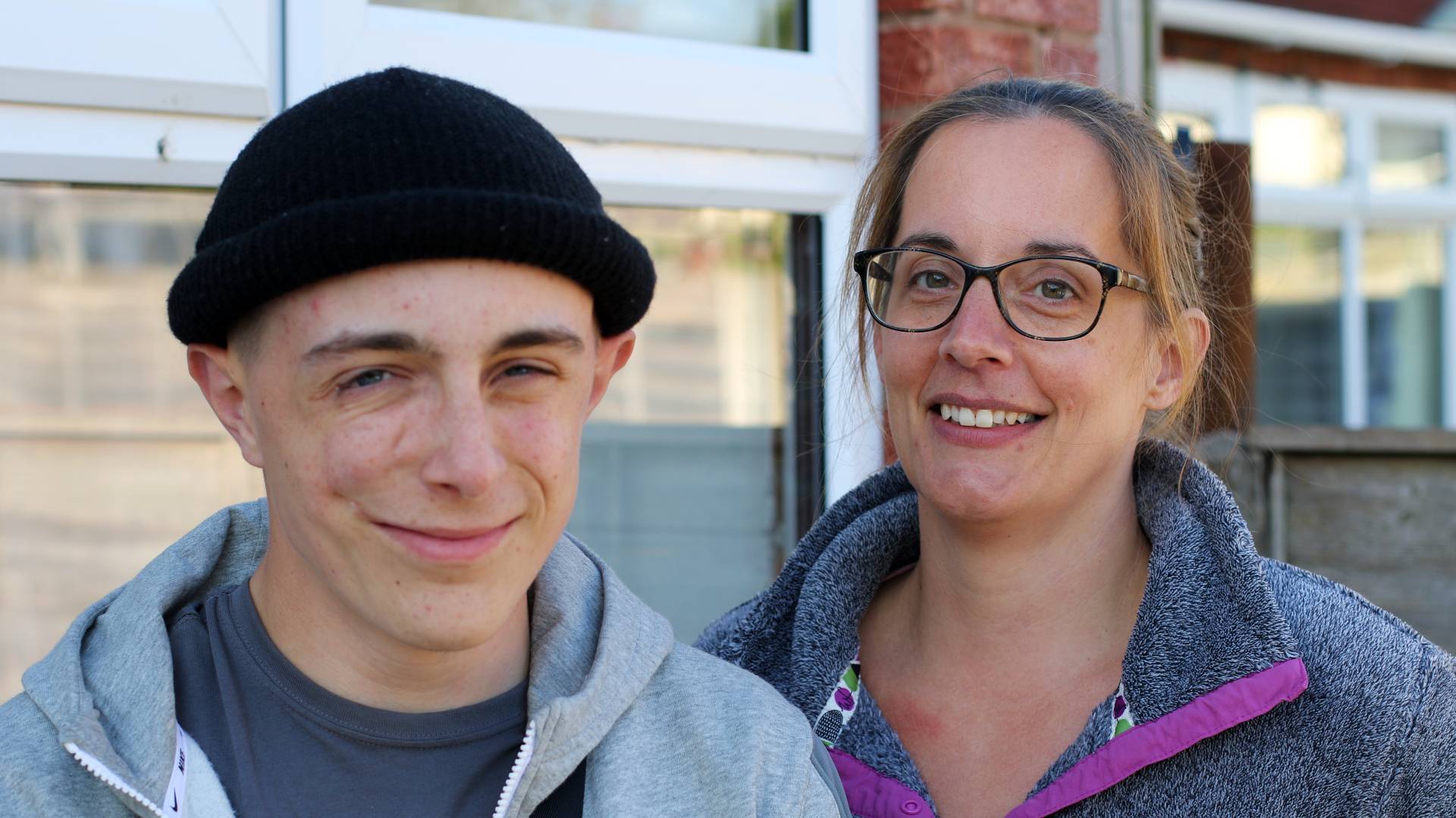 Marcus, who has facial scars on his face stands with his mother and smiles towards the camera.