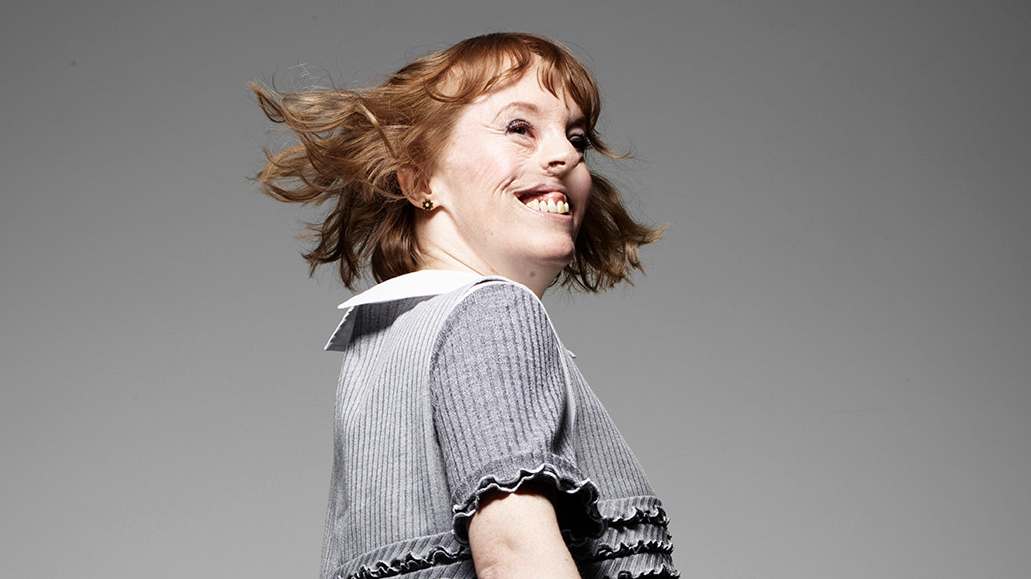 Amanda turning her head and smiling, wearing a black dress as part of the Portrait Positive photo shoot by Rankin