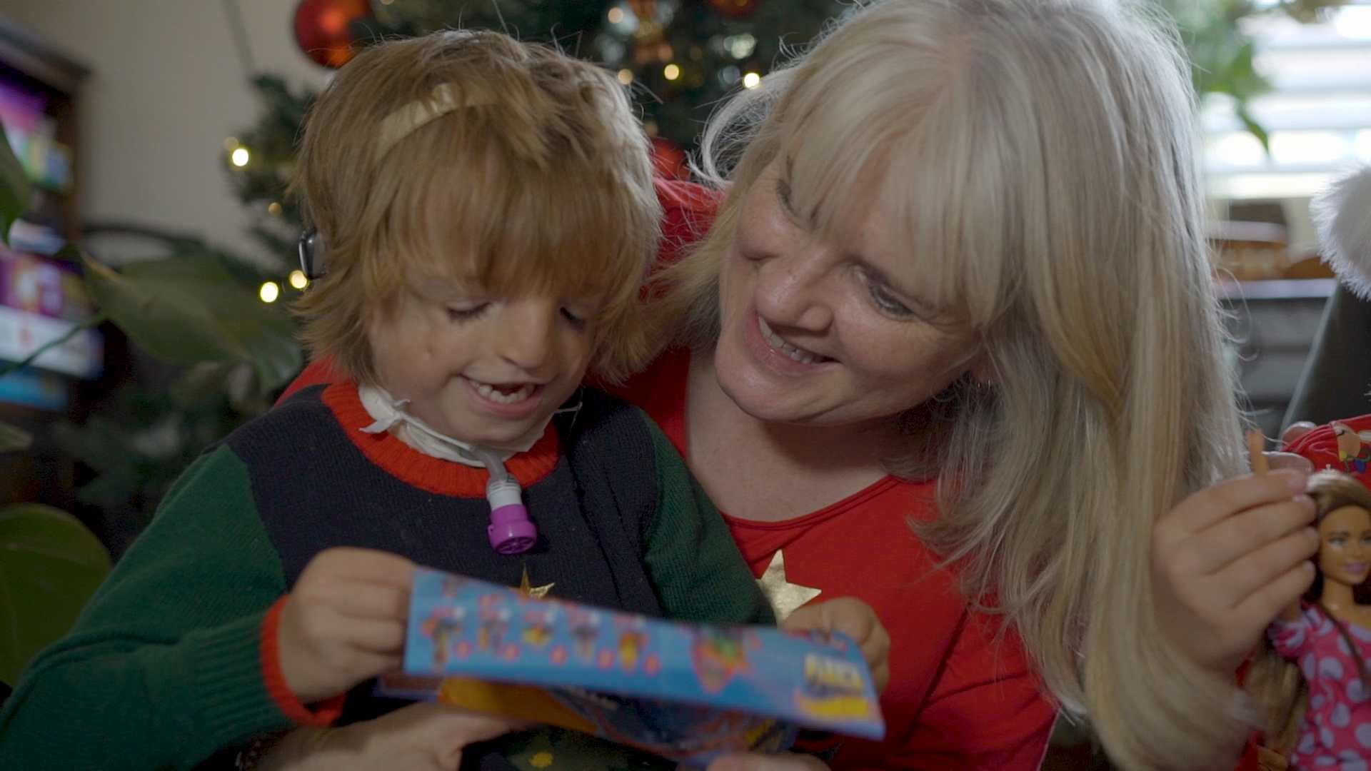 Kate holds her son, william, who is reading a book on her lap.