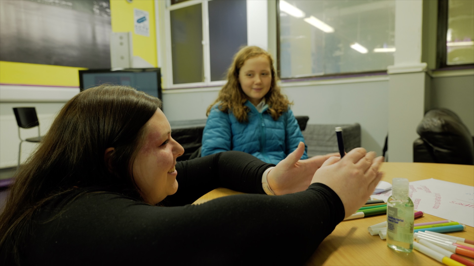 A youth worker with a birthmark works with young people seated at a table