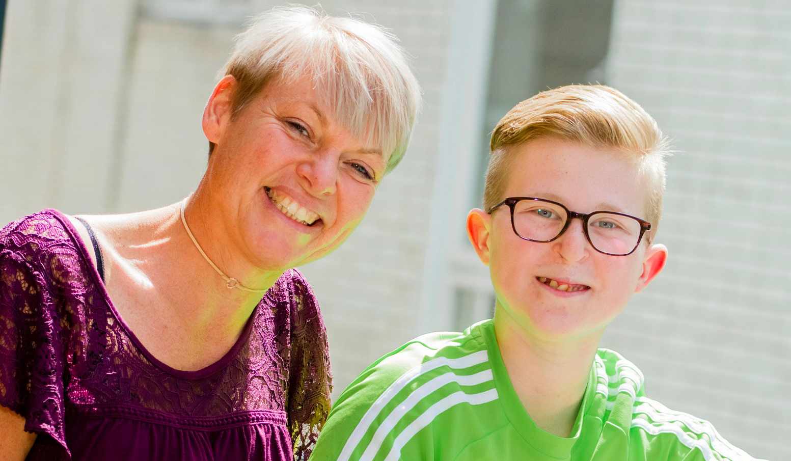 A woman and a boy with a cleft lip scar smiling, both looking towards the camera.