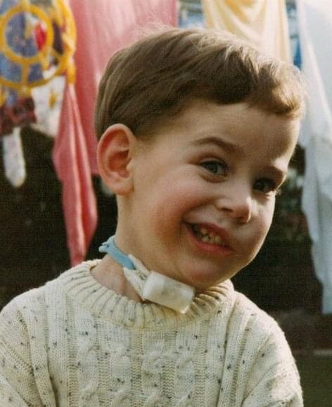 Athol as a seven year old boy. He has a tracheostomy and is wearing a white jumper.