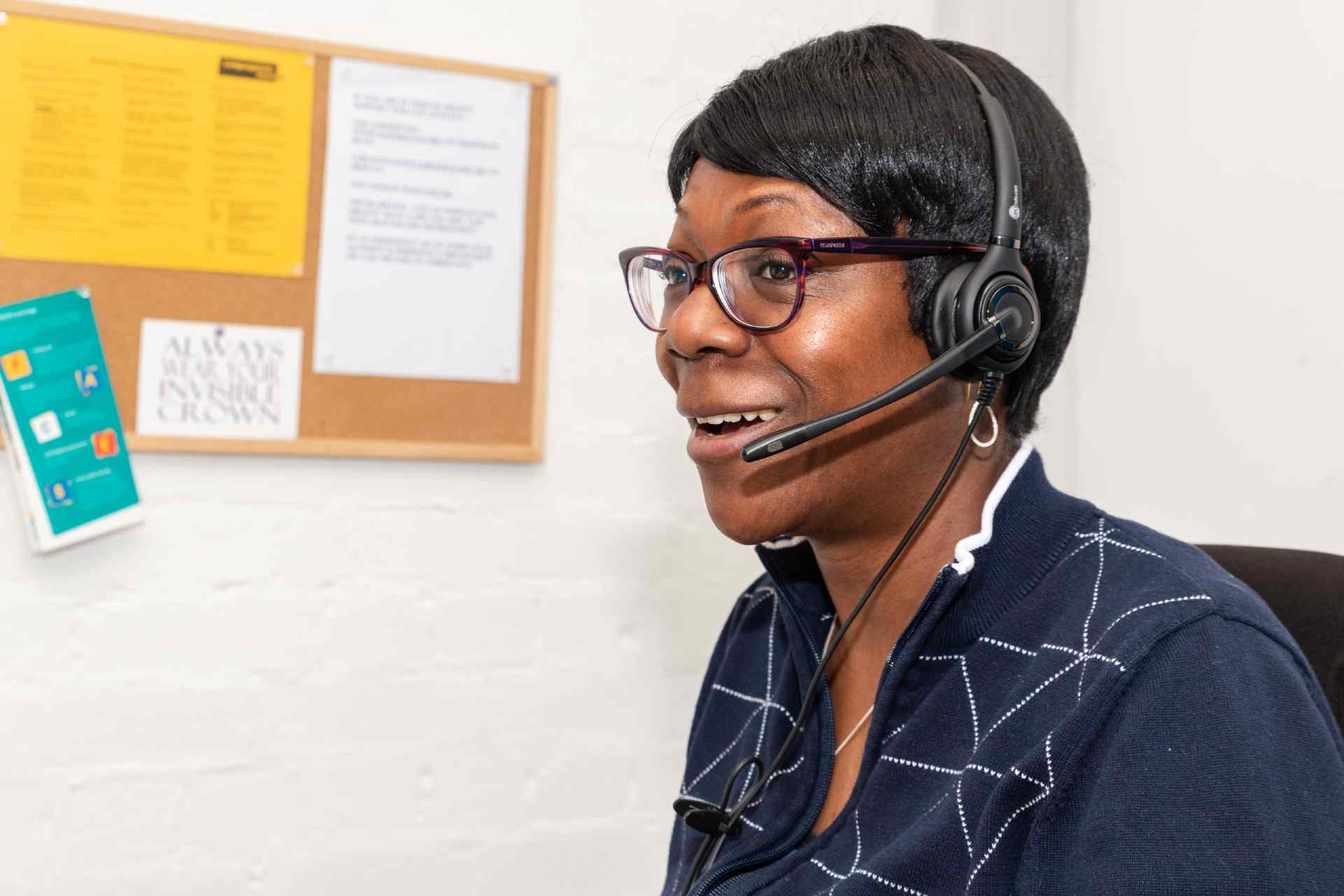Profile of a woman in an office environment, wearing a headset and smiling
