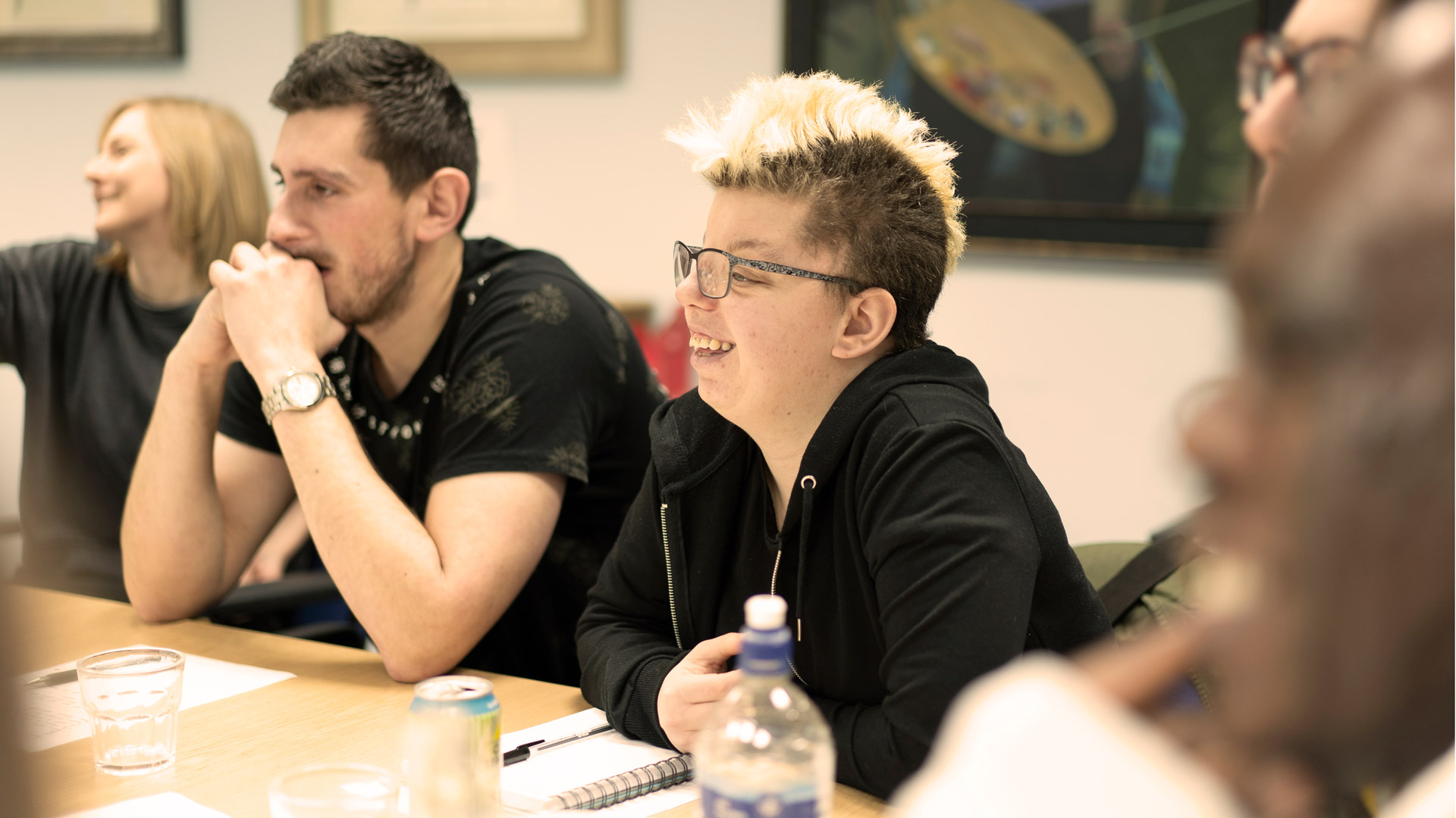 A group of young people stting around a table, smiling at someting to the side of the camera