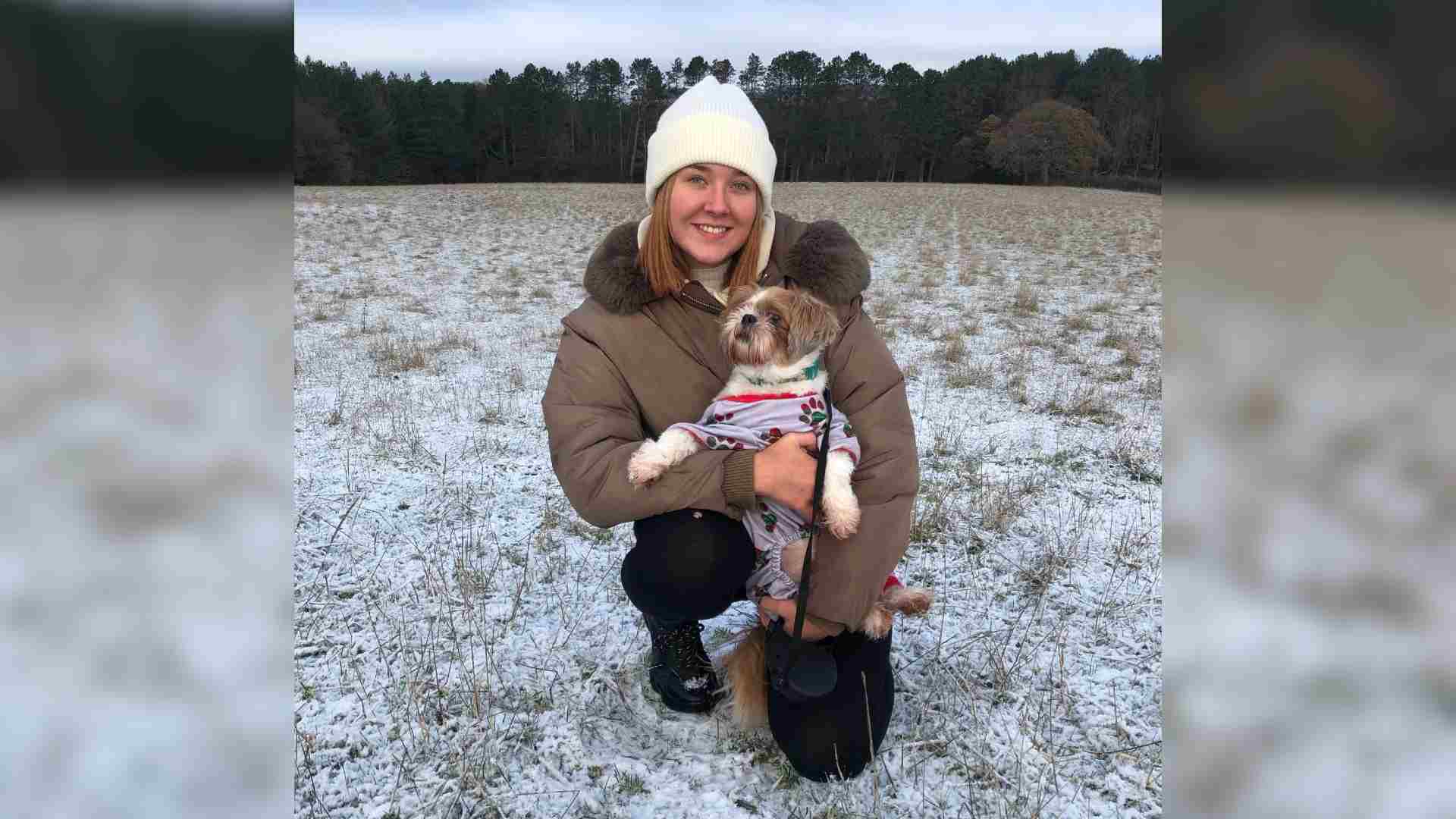 Woman crouches down in a snowy field with a small dog in her arms