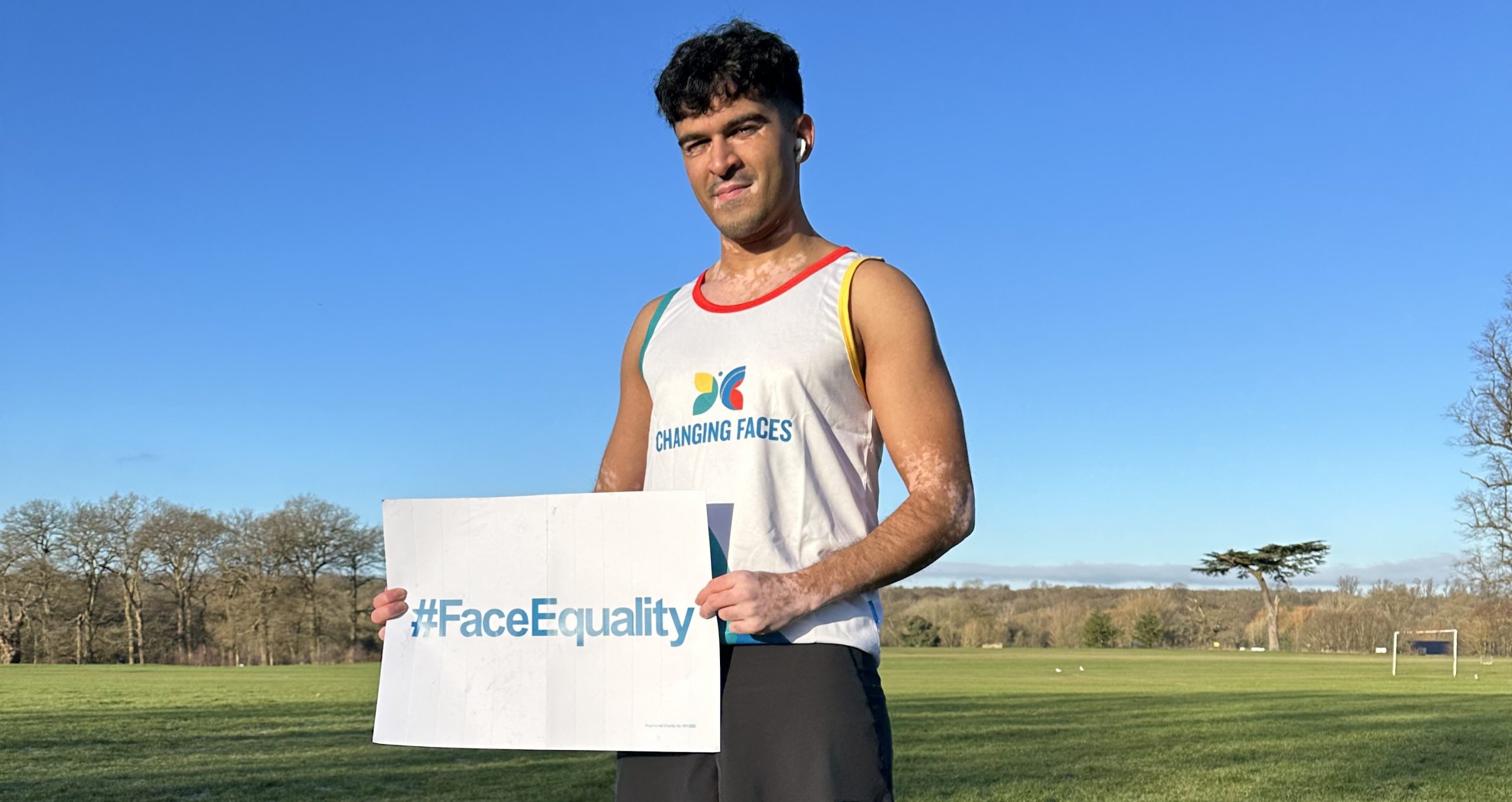 Sultan, one of our London Marathon runners who has vitiligo, standing in a field holding a #FaceEquality sign.