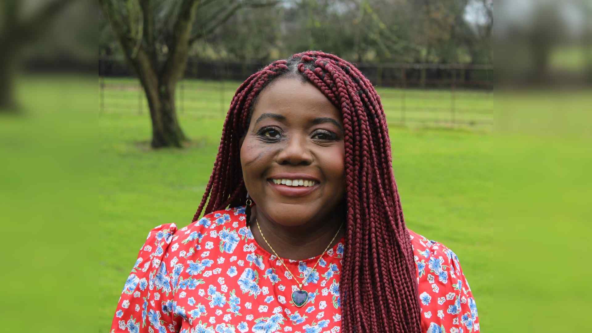 Tiwonge on Love My Face, the Channel 4 series. She has facial scarring and long red braided hair. Tiwonge smiles at the camera while standing in a rural setting.