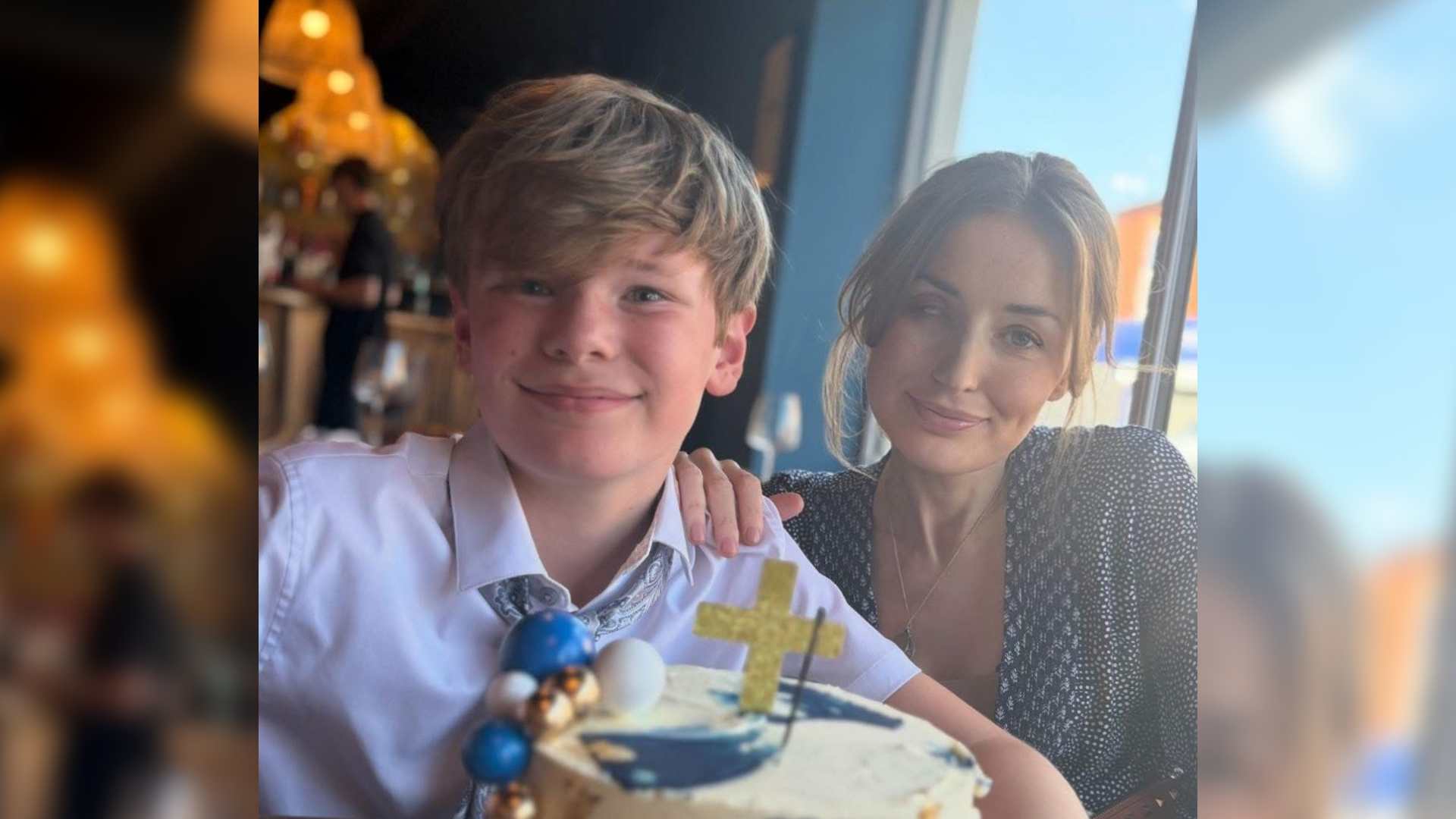 Becky is a parent with a visible difference - eye loss. She is sat next to her son with her hand on his shoulder. A celebration cake is in front of them.