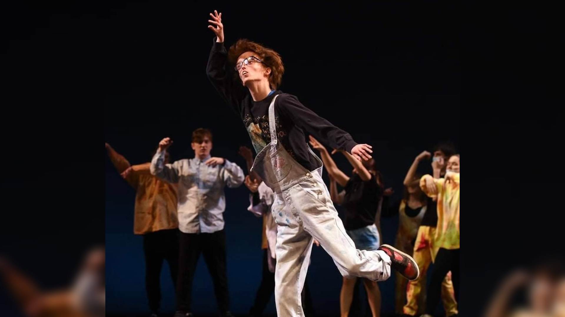 Dylan dancing on stage. He is reaching upwards with one arm while standing on one leg. Dylan has learnt to love himself through dance.