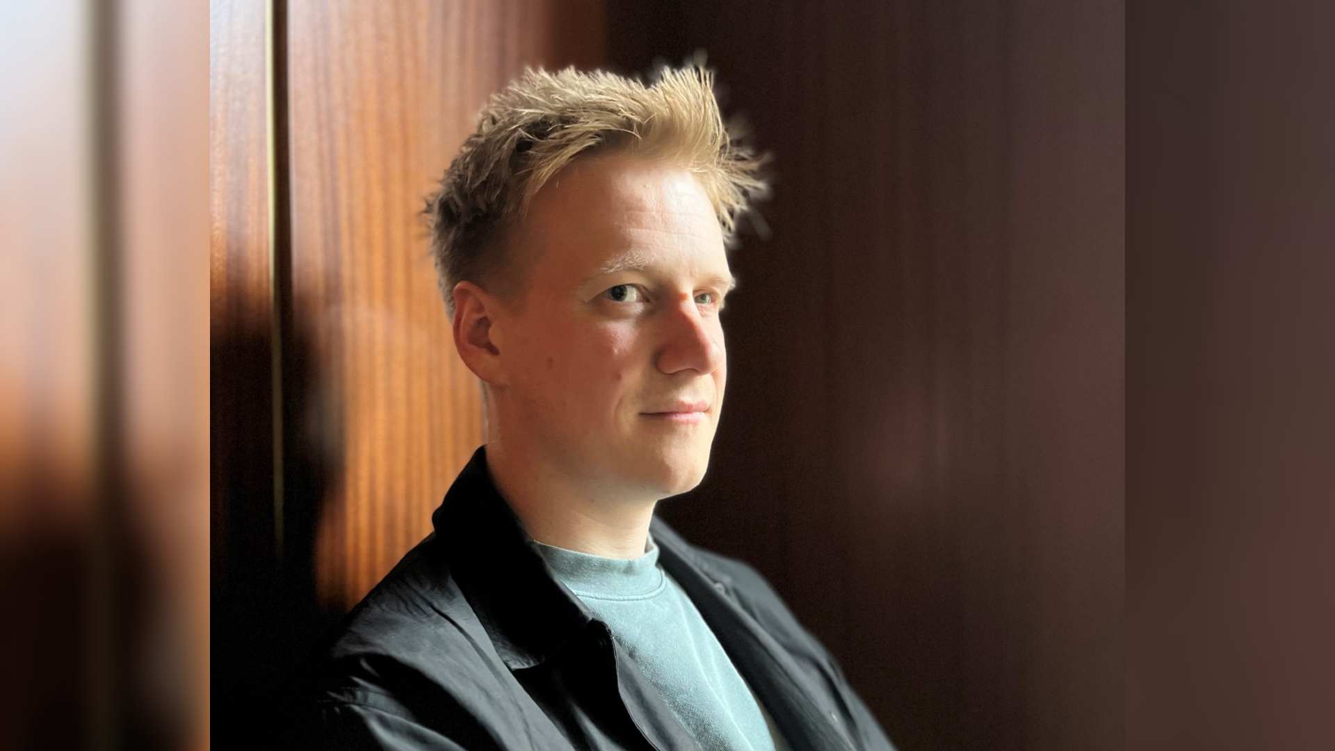 Hugo faces side on to the camera with his face turned towards the lens. He has short blonde hair and wears a blue t-shirt and black blazer. This is the hero image for Hugo's blog "Overcoming the shame around my scar"