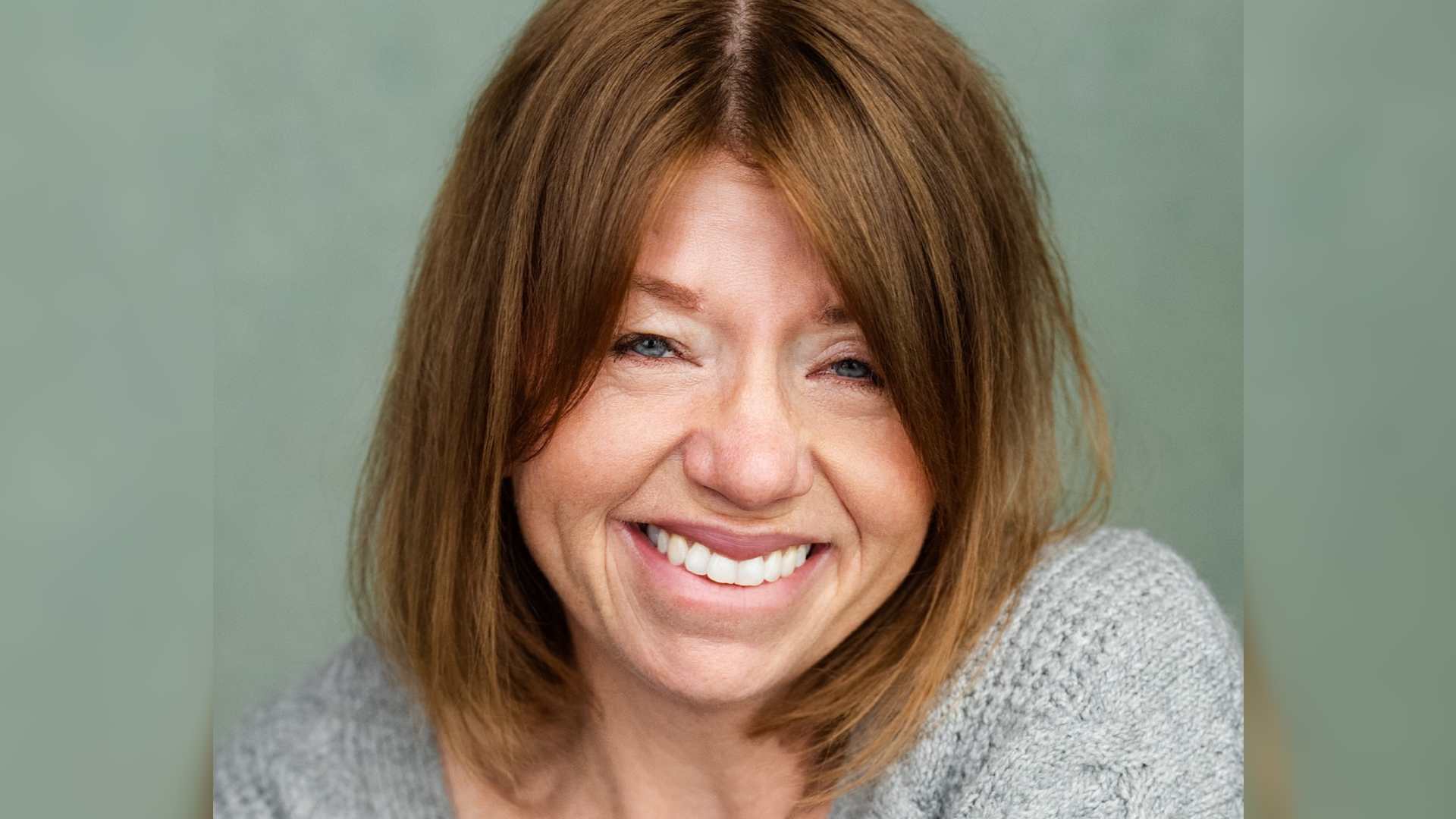 Gemma is a white woman with shoulder length hair. She smiles brightly at the camera. Gemma has ptosis due to Noonan syndrome.
