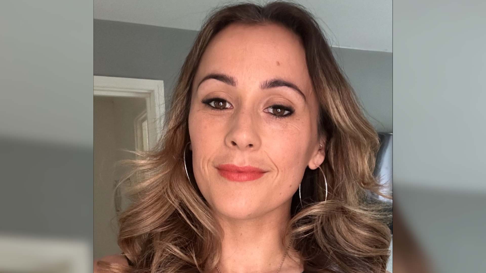 Carla has hyperpigmentation on her face, above her lip. Carla has long wavy hair and is smiling.
