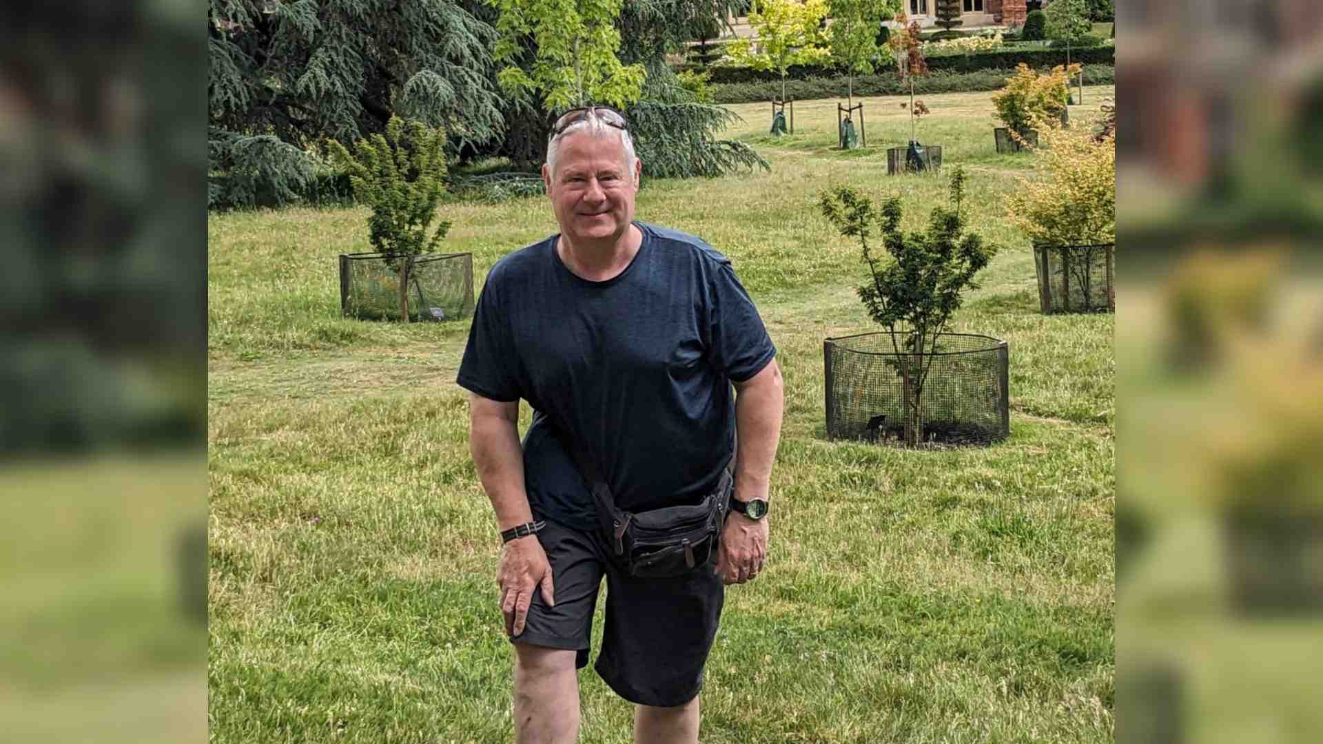 John has a Cavernous Haemangioma Lymphangioma and scoliosis. He stand on a large lawn surrounding by shrubs and trees.