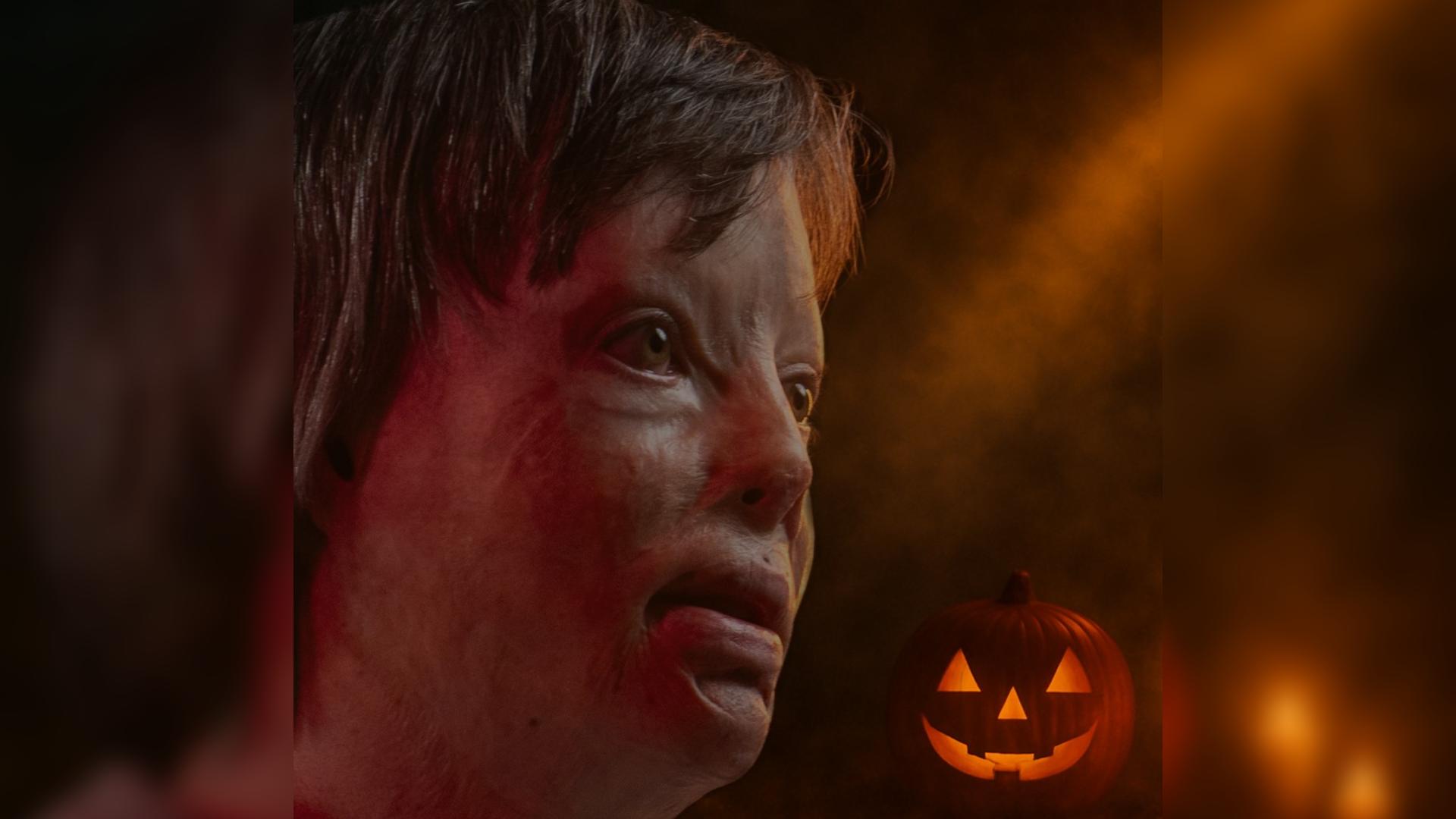 Marc looks off to the side - he has facial burns. The background of the image has Halloween vibes with a carved pumkin and dark orange light.