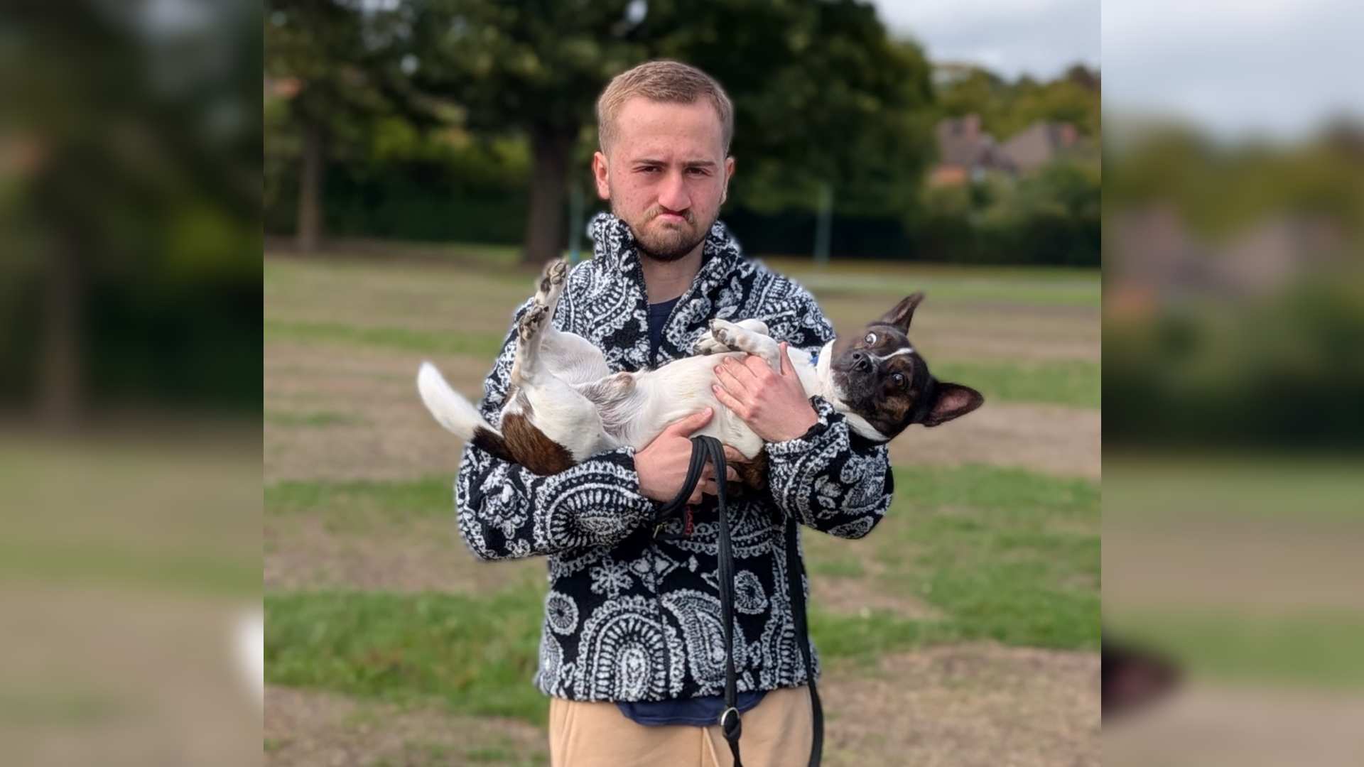 Enoch has a cleft lip and palate. He stands in a park holding a black and white dog.