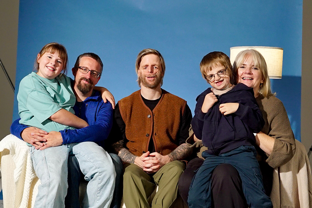 Jono sits on a sofa between Williams family