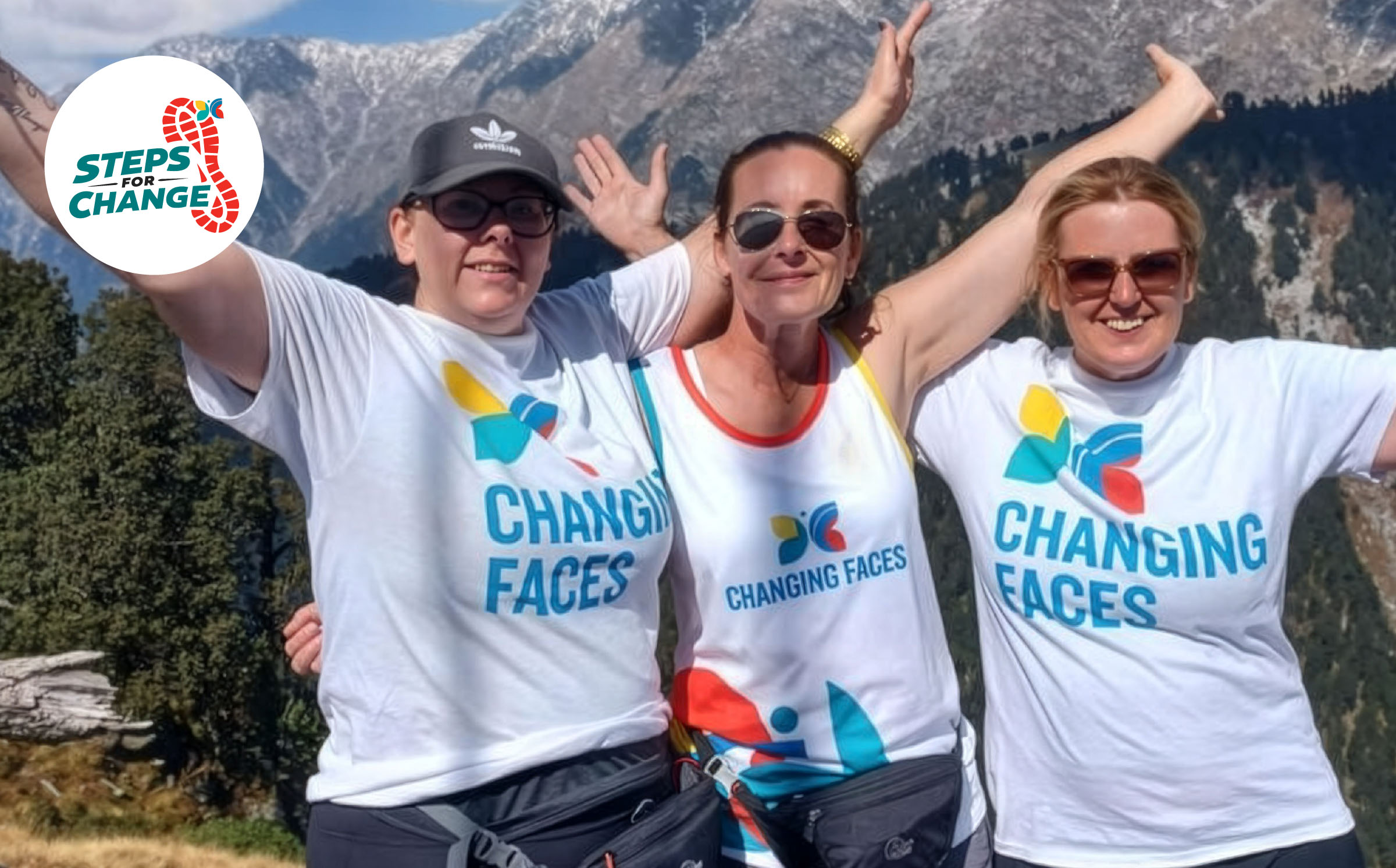 Three women with Changing Faces T-Shirts on stand with their hands in the air