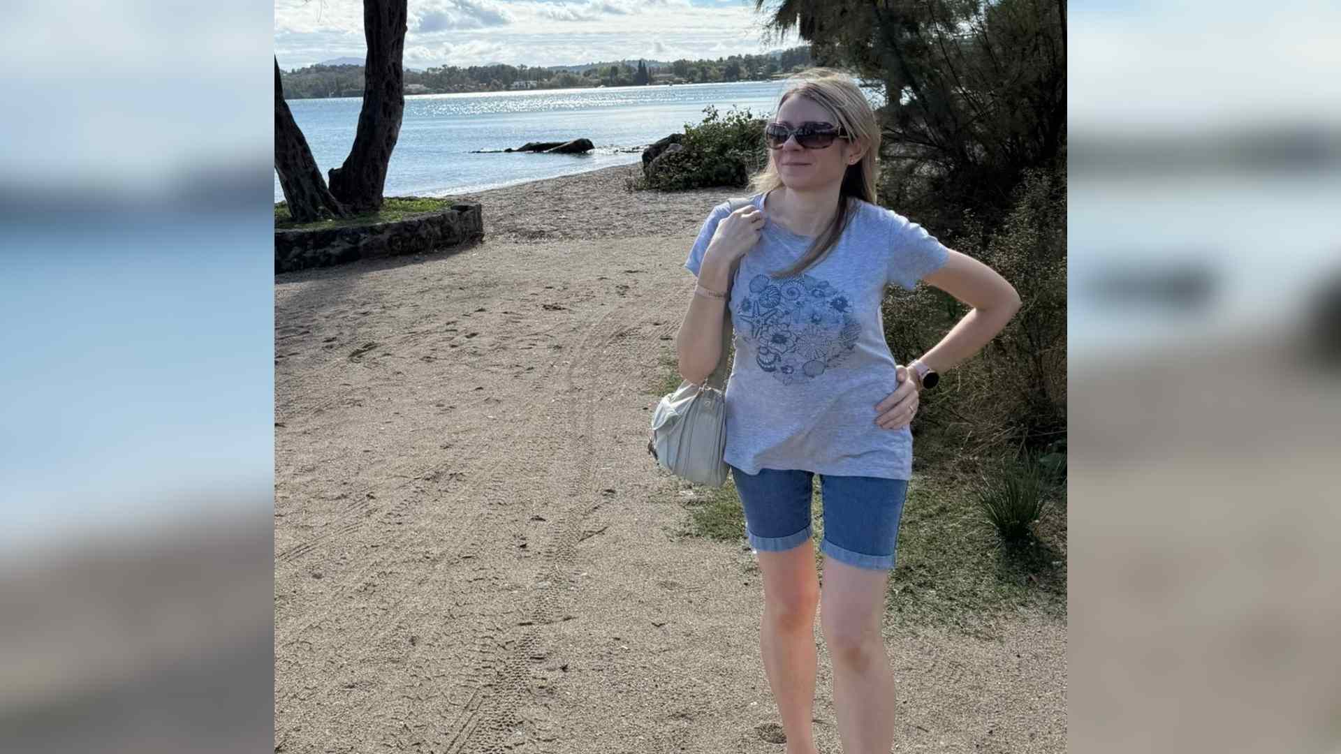 Corrina stands on a sandy beach with her hand on her hip. She has kyphoscoliosis.